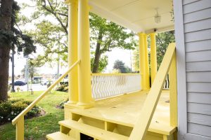 Sunlit yellow porch with white railings and columns at the Judith Holzman Law Offices, accessible to GTA clients.